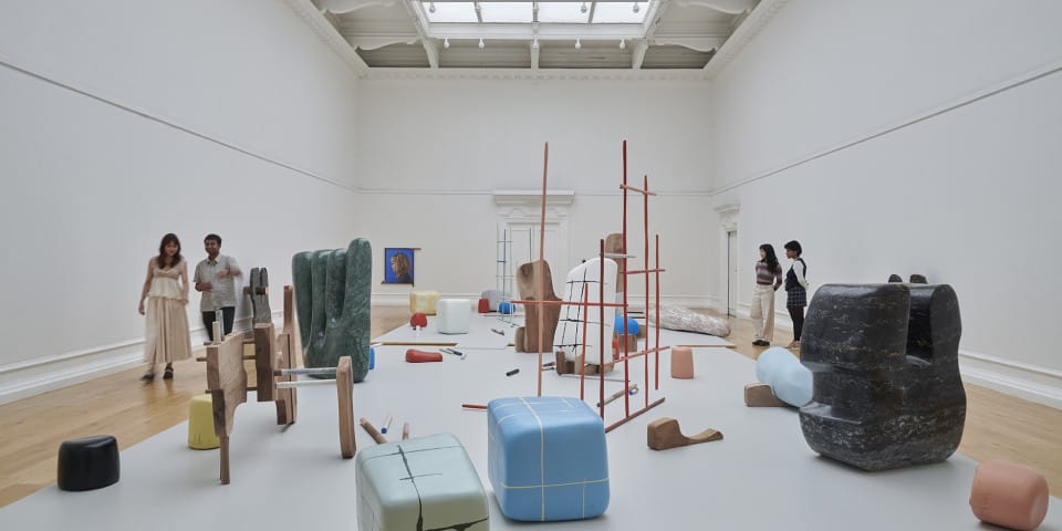 People walk around a large art gallery. They are looking at abstract sculptures and engaging with the art.