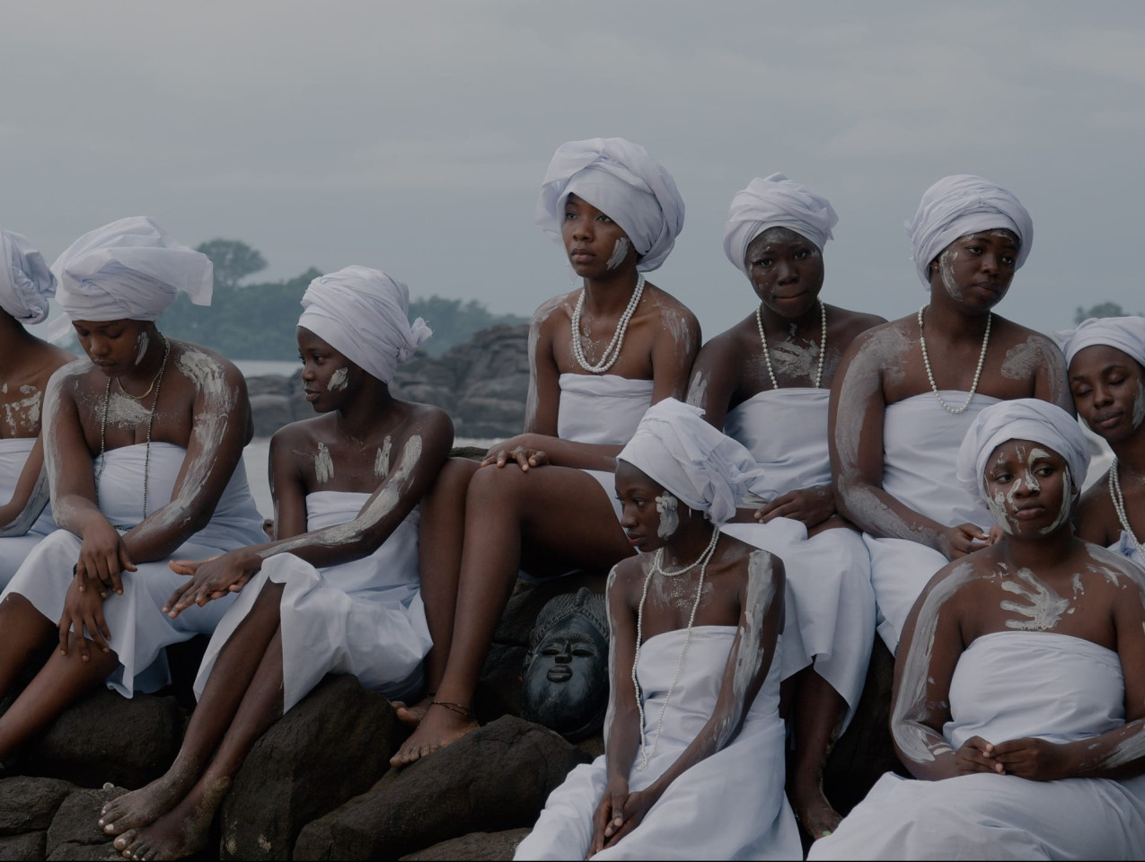A group of women wearing white and covered in white paint sit together.