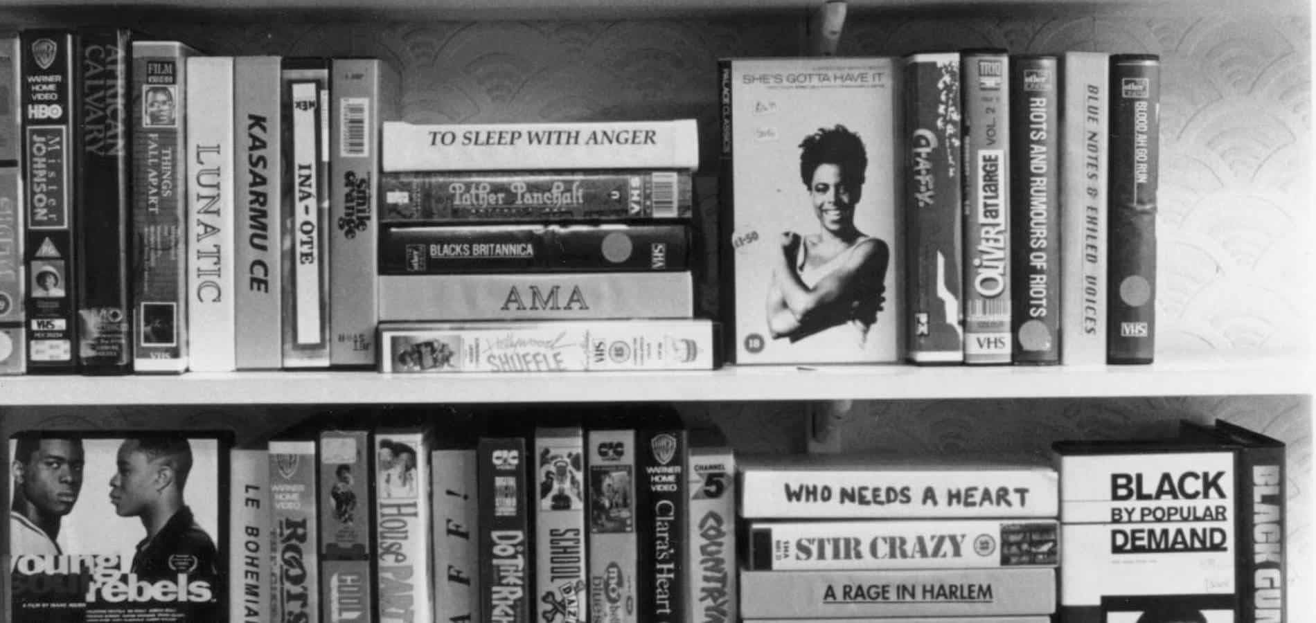 A black and white photo of book shelf with old books and videos.