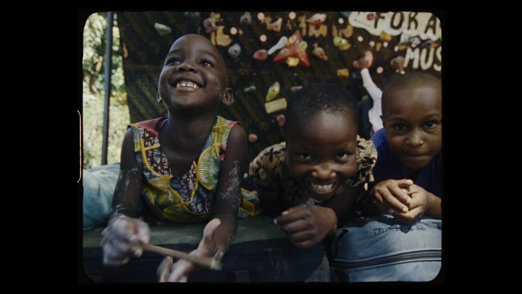 Three children sit together and smile and laugh.