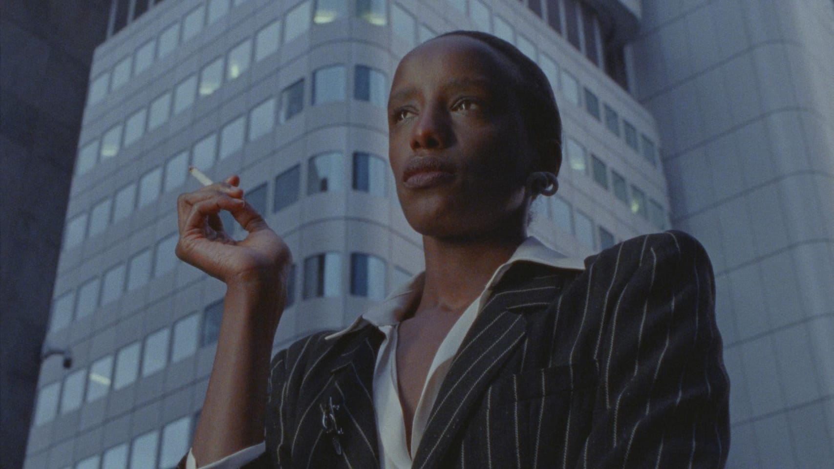 A person wearing a blazer stands under a sky scraper.
