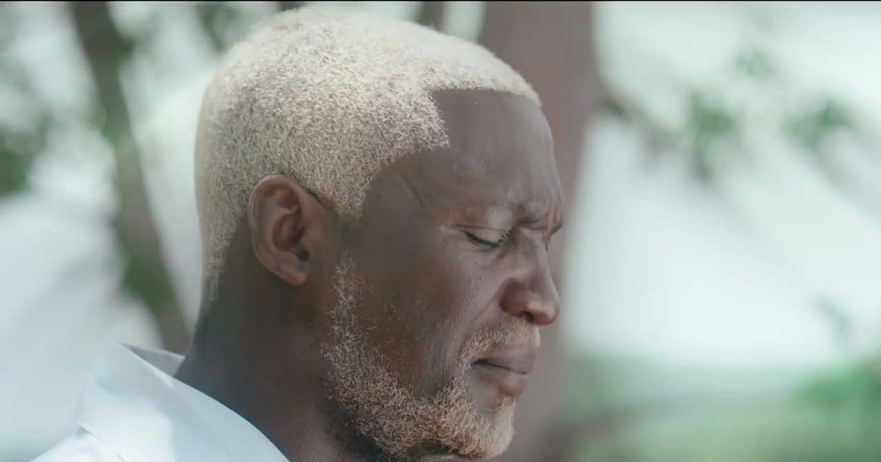 A close up shot of a man with white hair closing his eyes.
