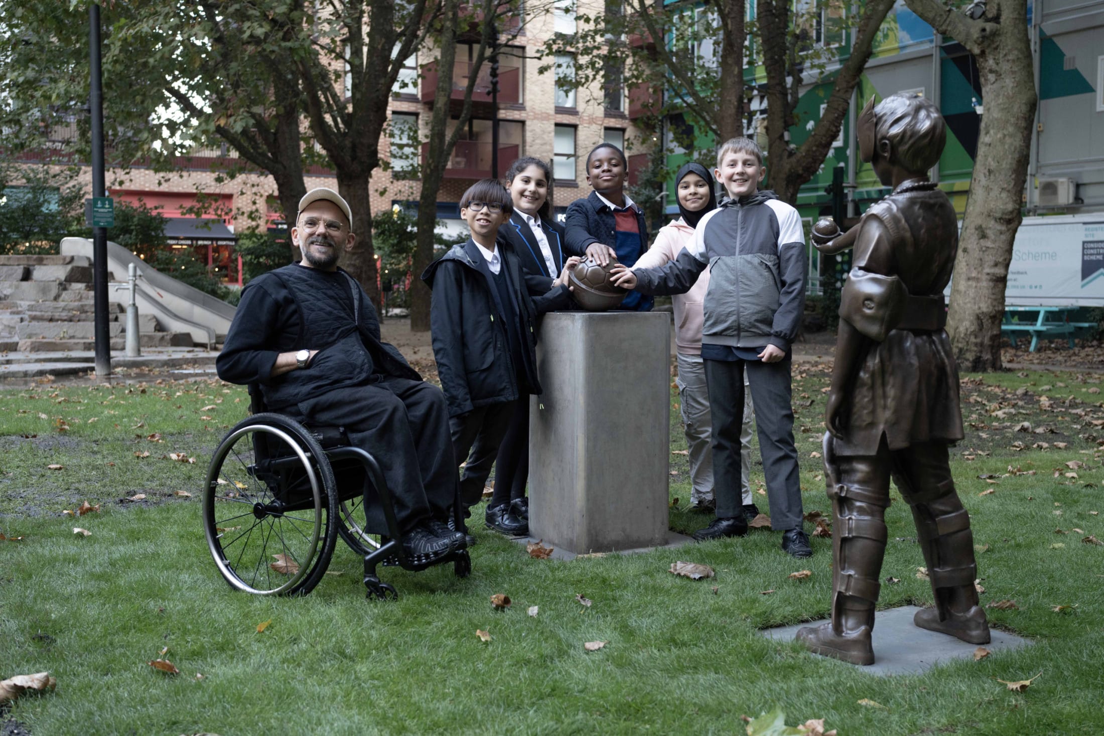 Children and artist Ryan Gander together, touching a bronze sculpture in a park in Elephant & Castle.