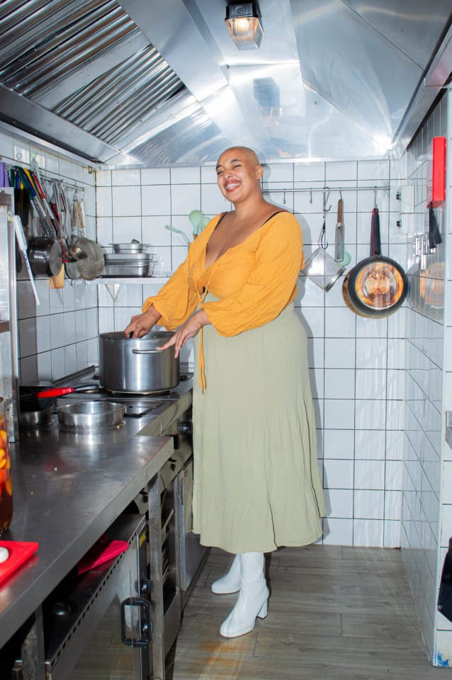 A person wearing a bright yellow top stands in a kitchen stirring something in a pot.