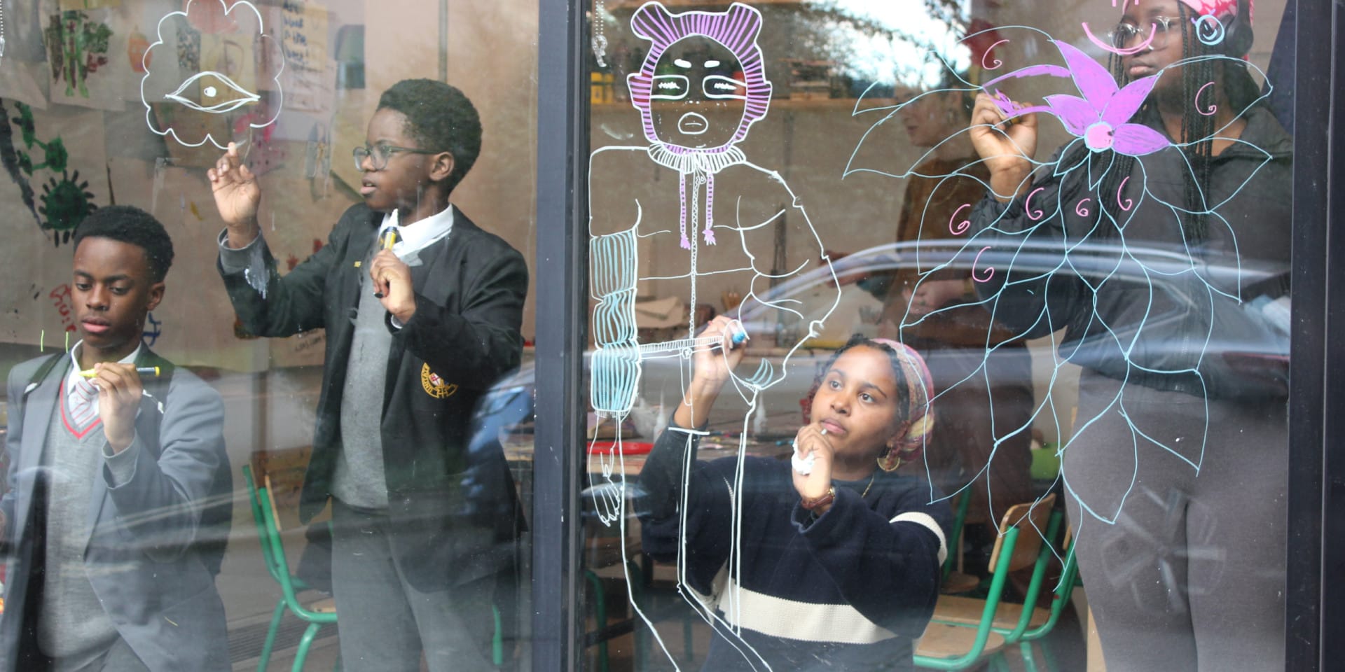 Children and young people draw with markers on a window.