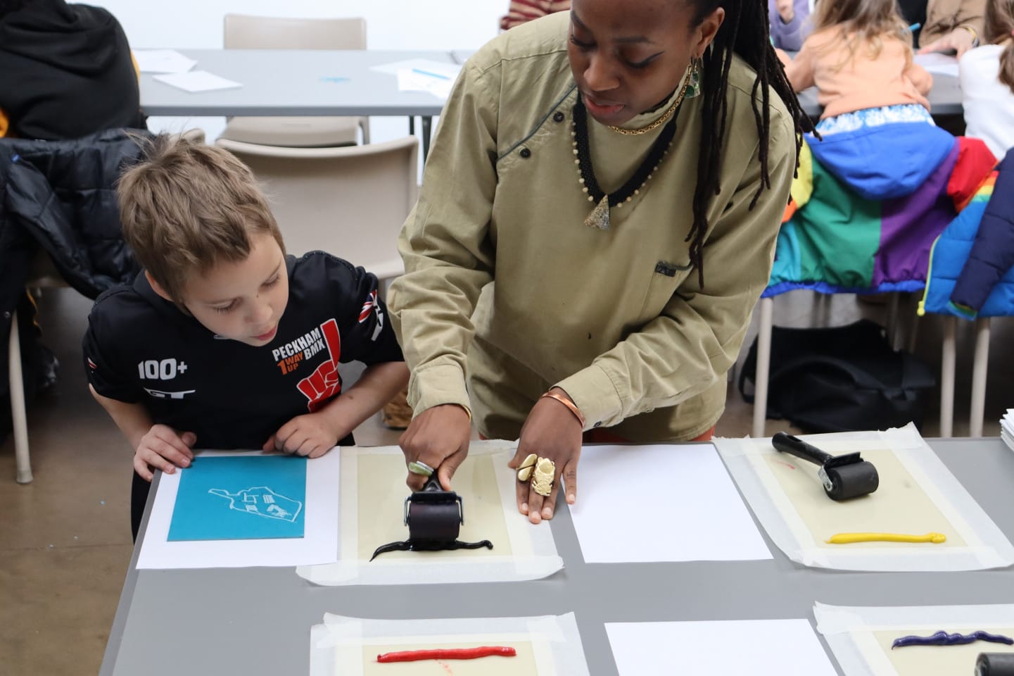 An artist works with a young child in a creative family workshop. They are doing lino printing.