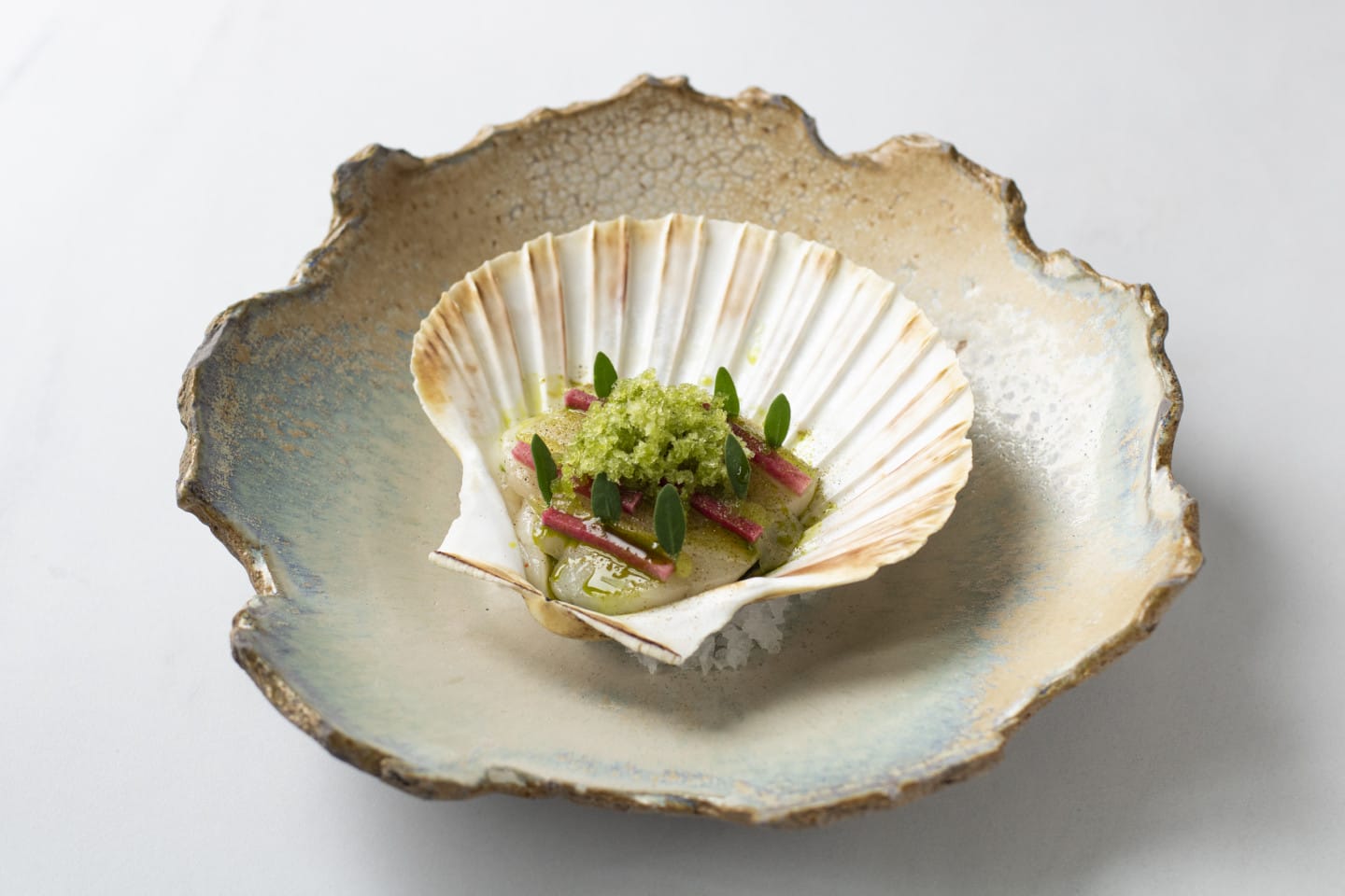 A plate of food made by Supper Club Gem. A garnished scallop is presented in a shell.