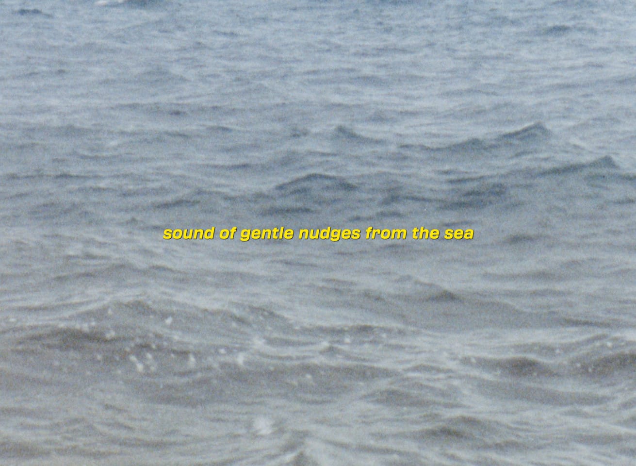 A still from a film, Seo Hye Lee, Portland Forecast, 2024. The still shows a photo of the sea. Over it is text, which says: sounds of gentle nudges from the sea.