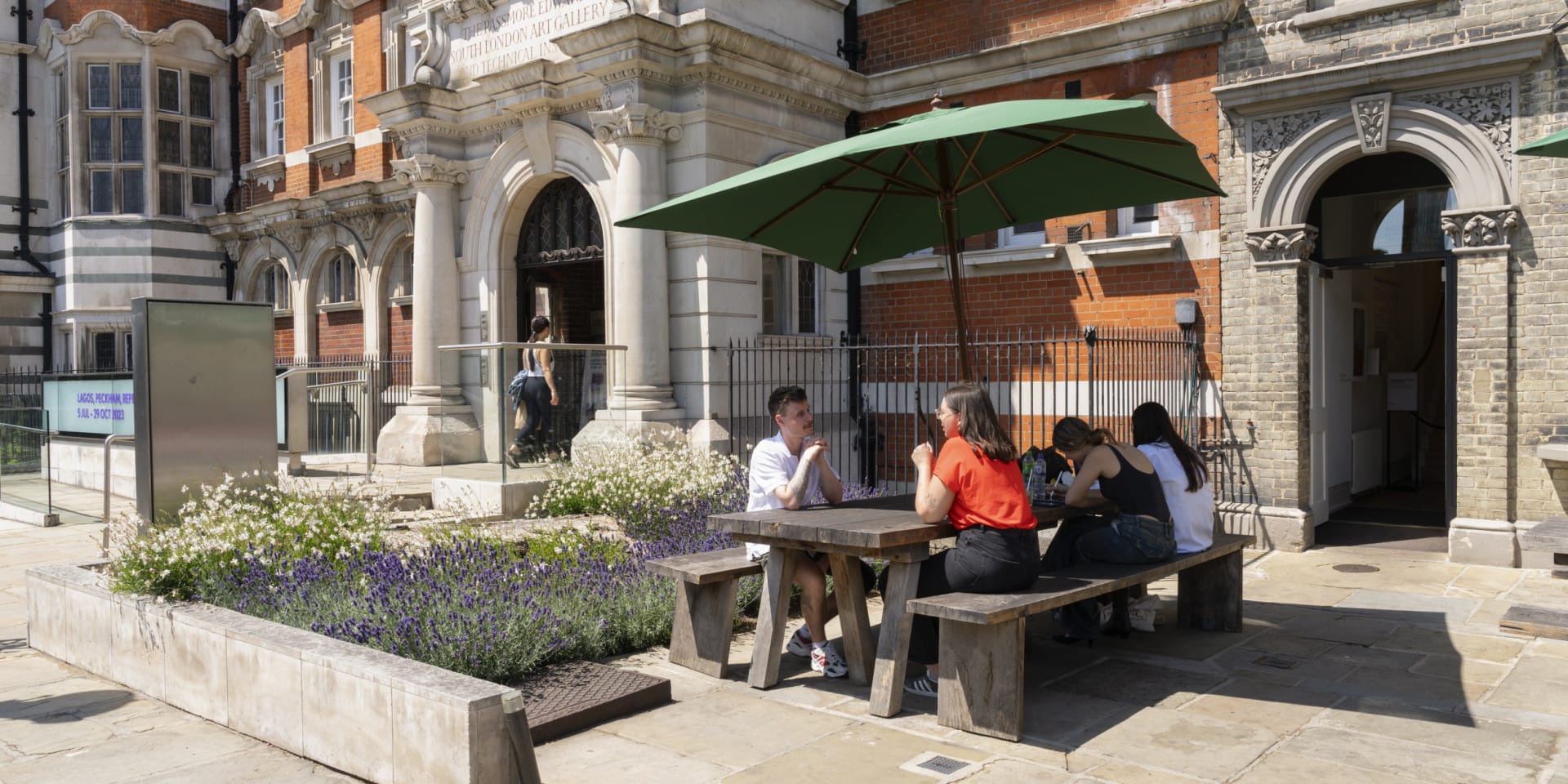 People sit at tables outside a large red brick building.
