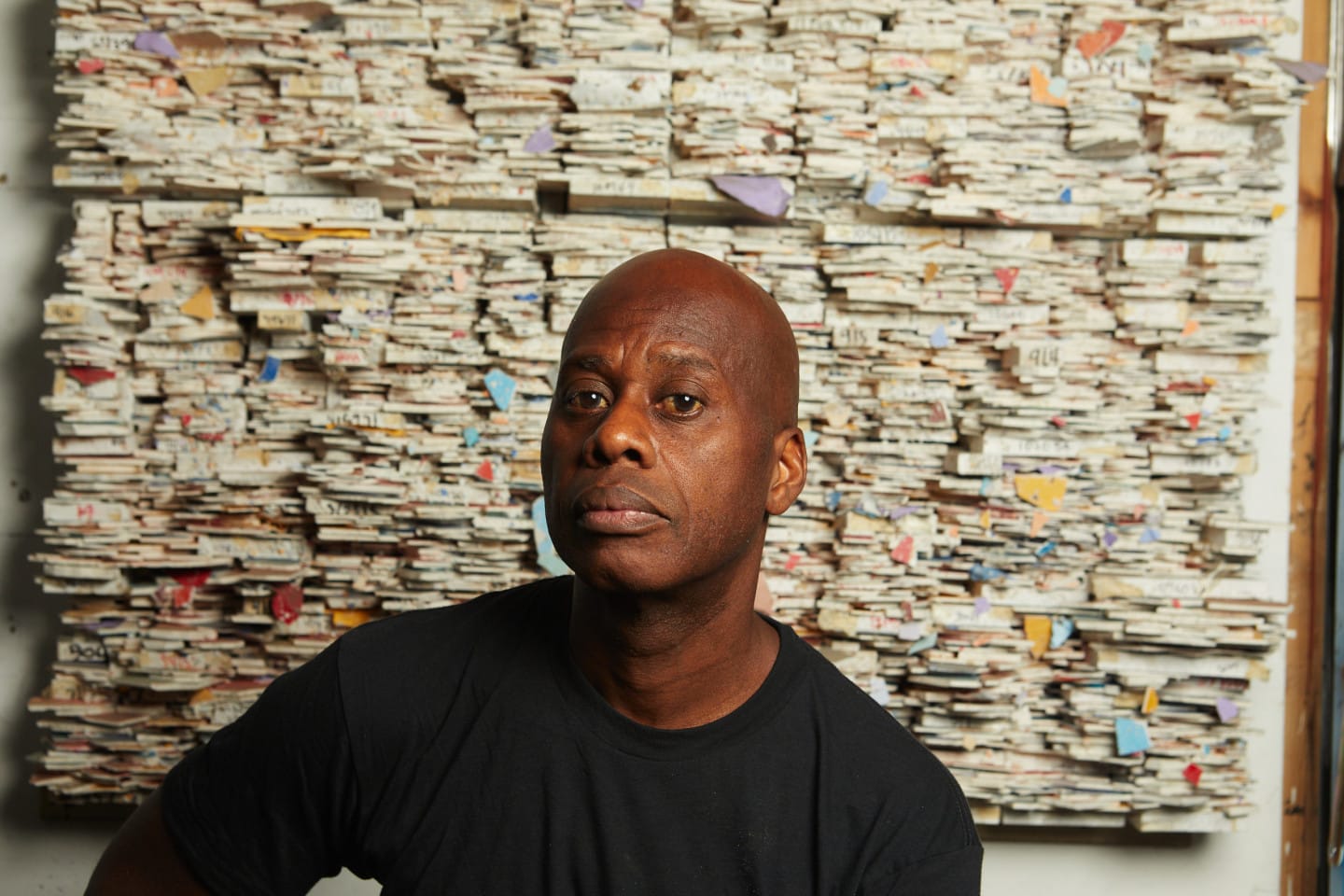 Artist Leonardo Drew sits in front of an abstract work of art in his studio.