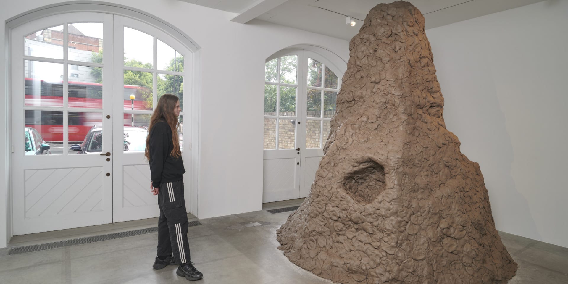 An installation by artist Damian Ortega at the South London Gallery. A person stands looking at a large scale sculpture made of clay. The sculpture is in the shape of a mountain,