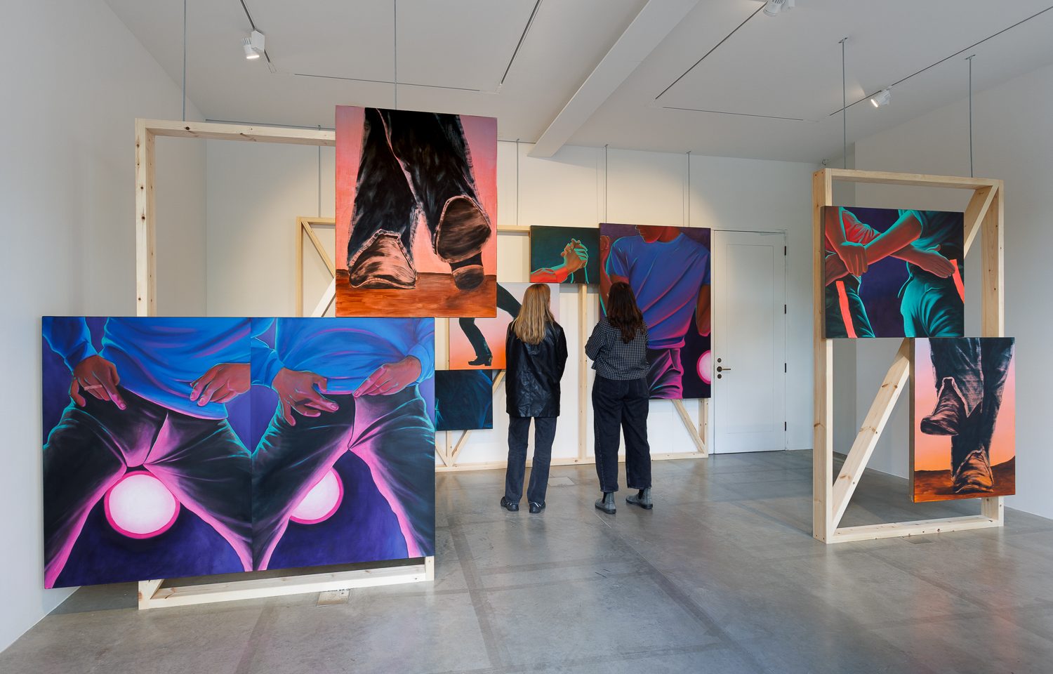 Two people stand in an art gallery and look at paintings by Ana Segovia.