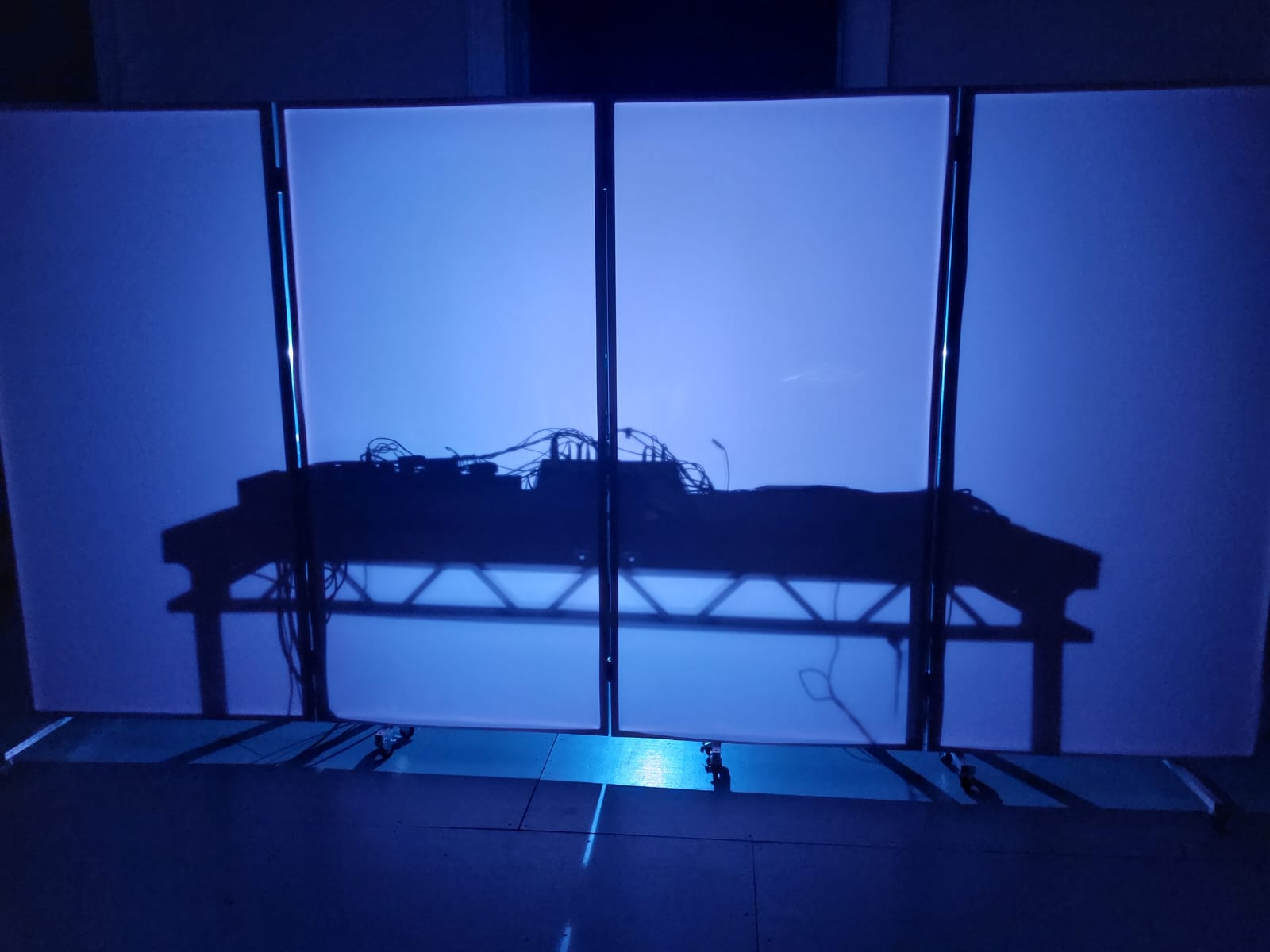 A DJ deck, backlit behind a screen. The purple light behind the decks, projects a silhouette of the table onto the screen. This is from a performance at Somerset House by artist Appau Jnr Boakye-Yiadom