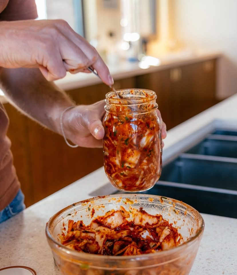 A person adds kimchi to a jar.