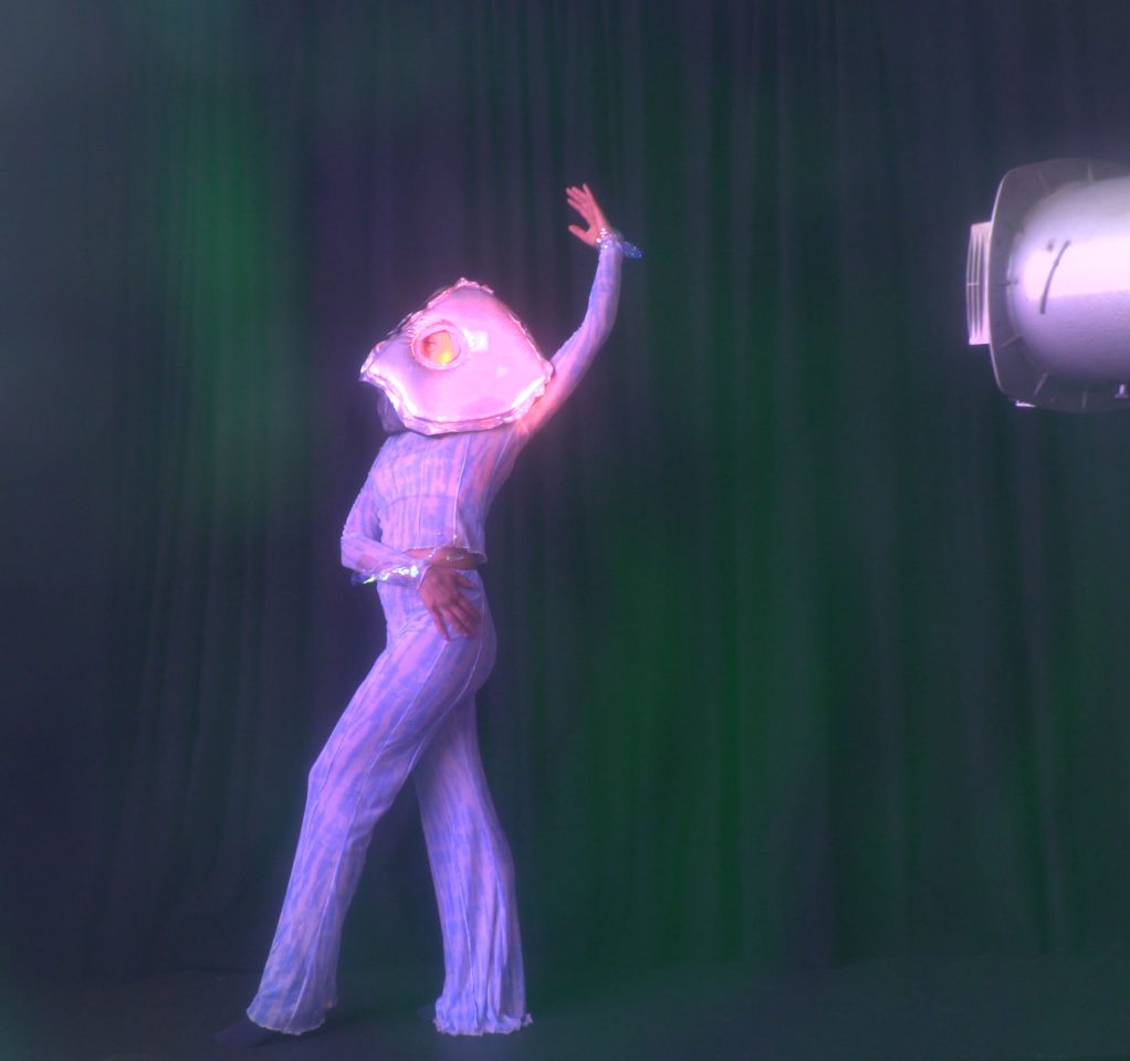 Artist Krystle Patel performs with a silver fish head costume on.