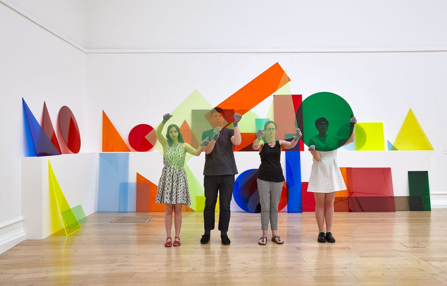 People stand in a gallery and hold up colourful shapes.