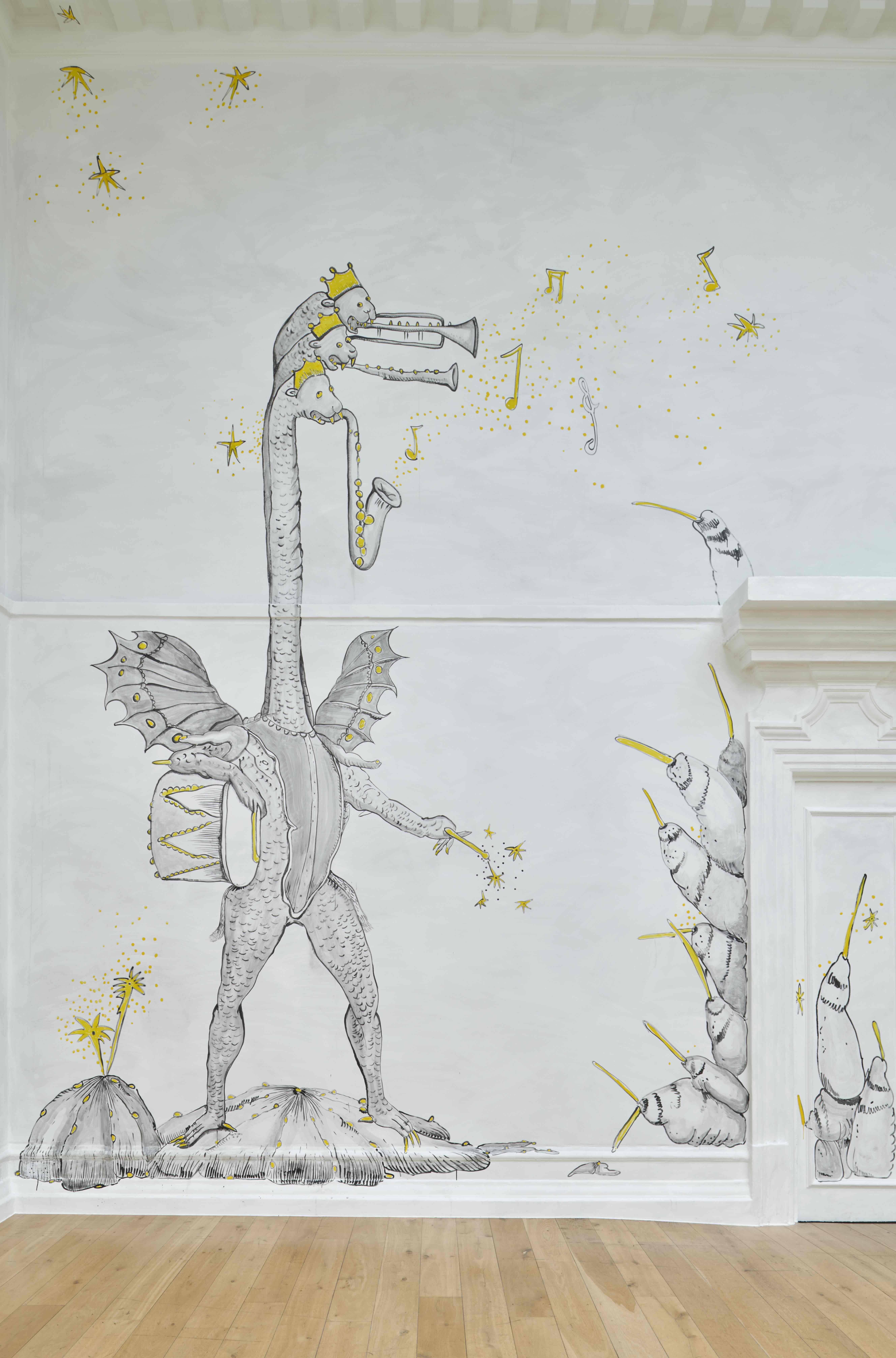 A wall drawing in a gallery depicts a fantastical creature with a long neck and wings, standing upright and playing multiple trumpet-like instruments. Musical notes and star-shaped bursts in yellow float around the figure. The monochrome drawing with yellow highlights is set against a pale grey wall with decorative architectural details and a wooden floor.