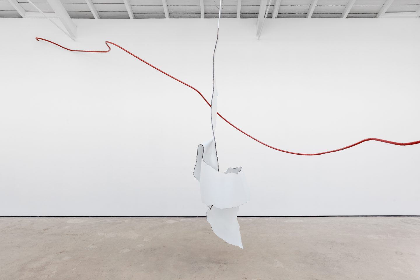 Installation view of a gallery. In the middle is a sculpture consisting of a thick red metal pole running in an undulating line and a torn white sheet of metal hanging from the ceiling.