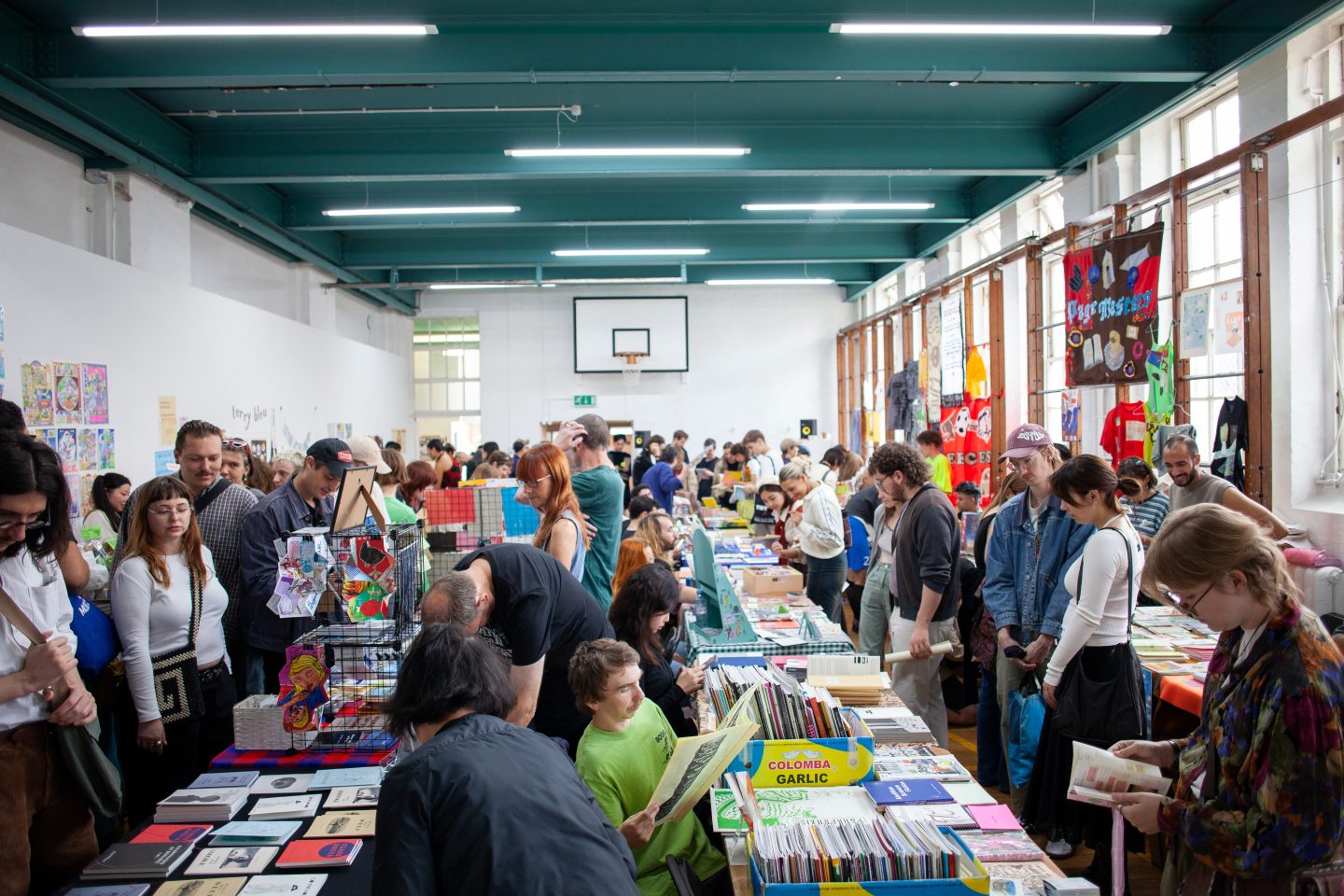 A busy room full of tables with books on them, people are looking through the books.