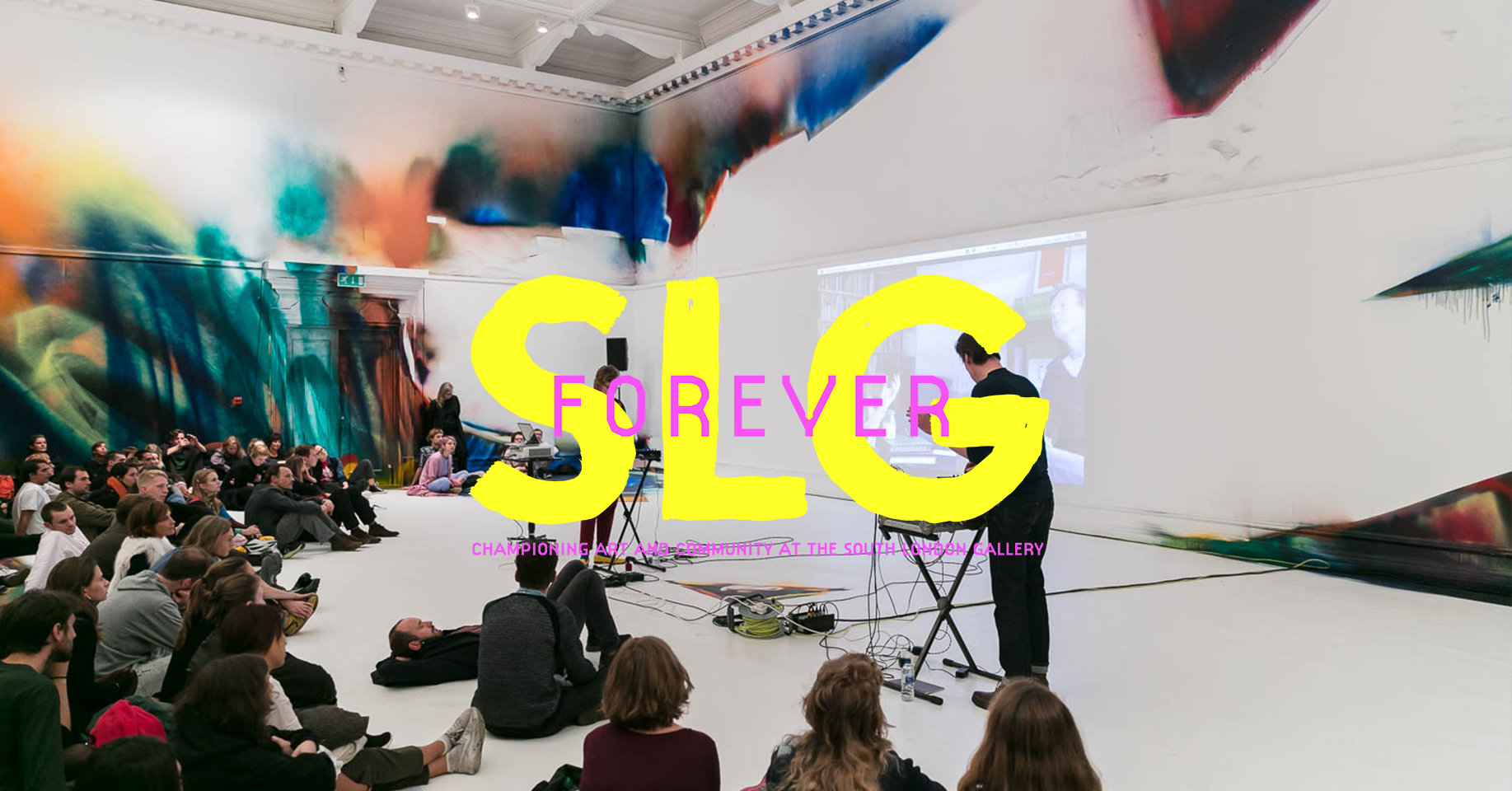 A photo of an event in the main gallery, the walls are painted with art, there are people playing the keyboard and people watching. A logo is superimposed that says SLG Forever, and is for the 135th anniversary fundraising campaign.