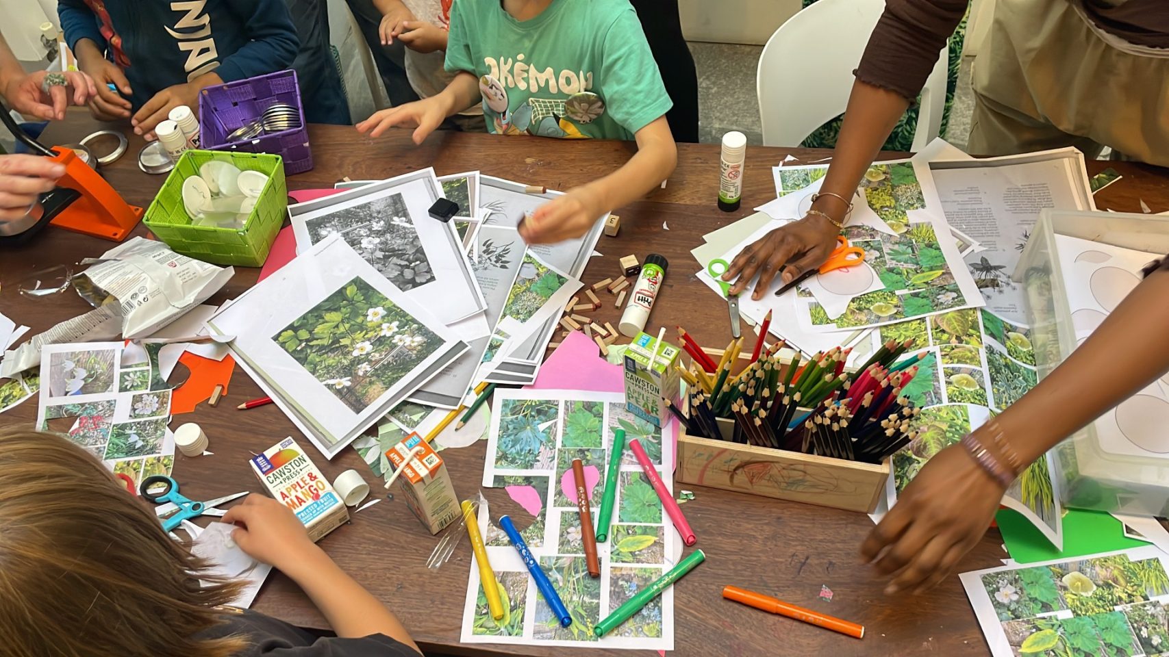 Children and adults partaking in workshop around large table with lots of paper resources, colouring pencils and supplies.